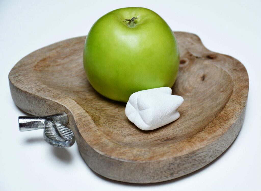 a green apple and a white tooth on a wooden plate